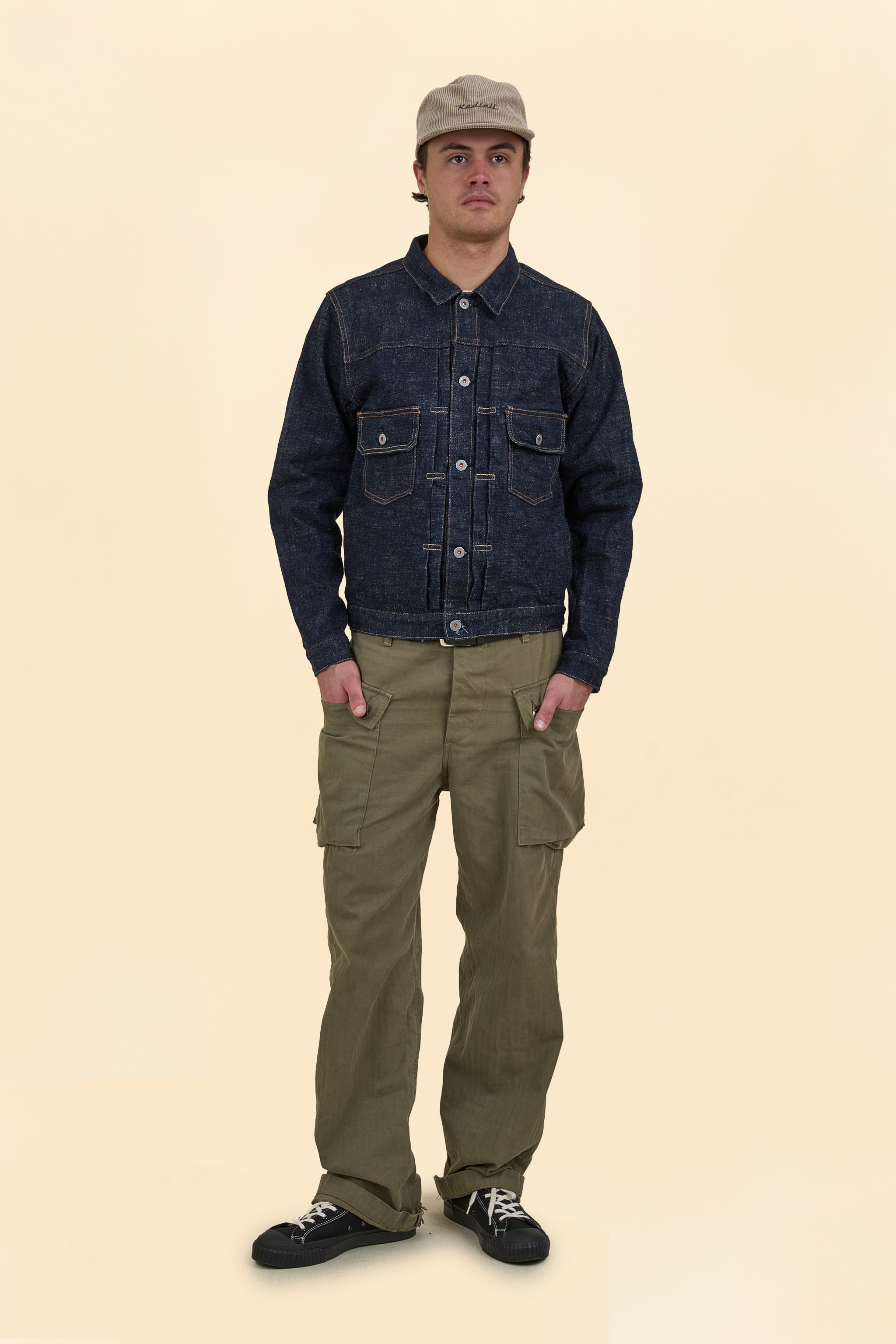 Man wearing a dark denim jacket and olive green pants on a beige background
